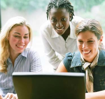 Three women sharing laptop computer at workplace